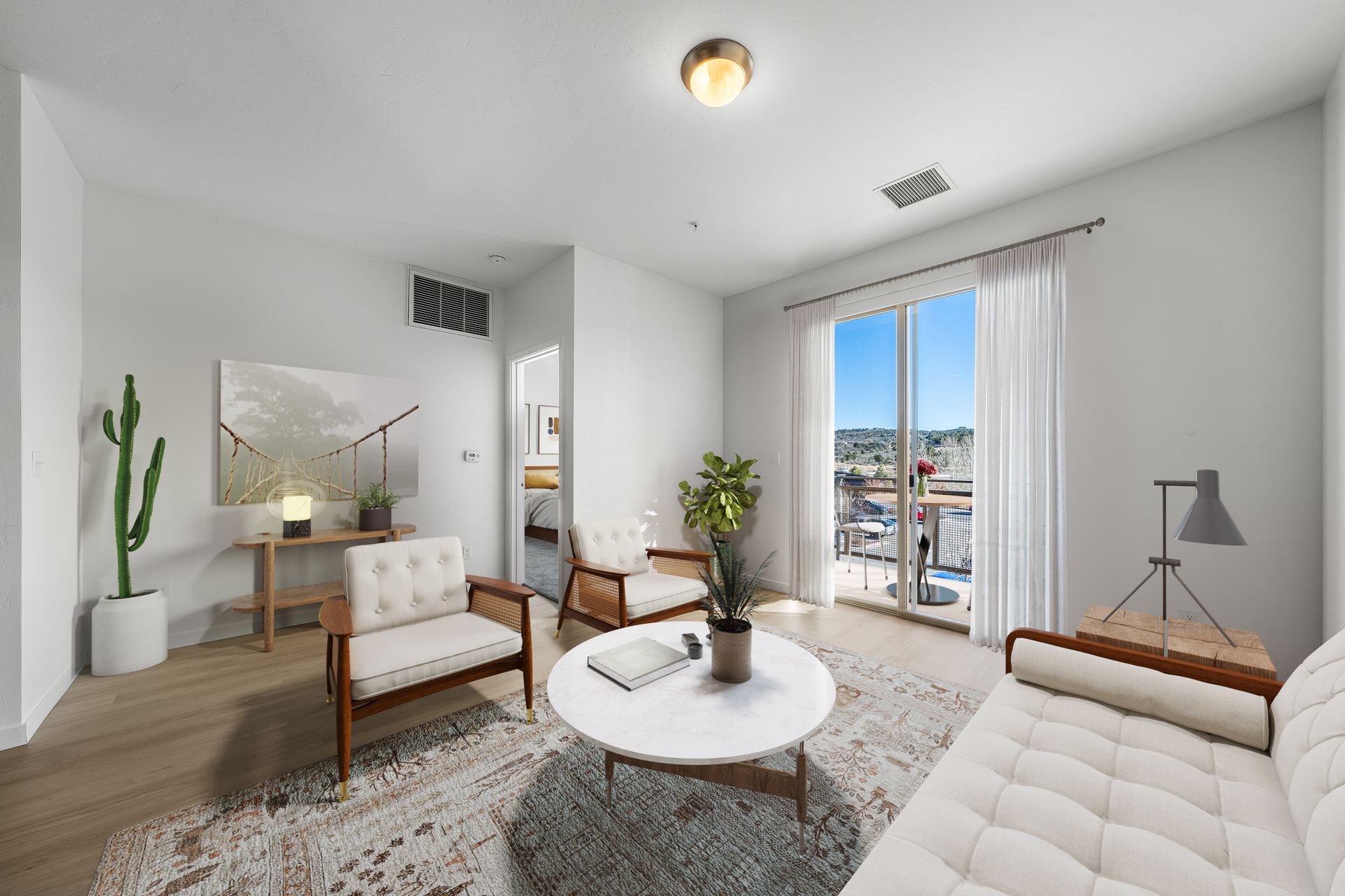 Bright living area with white walls, mid-century chairs, and a sliding glass door to a balcony.