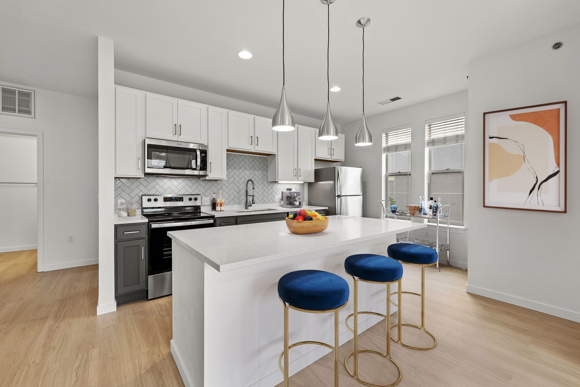 Modern kitchen in an apartment with white cabinets, stainless appliances, and a large island.