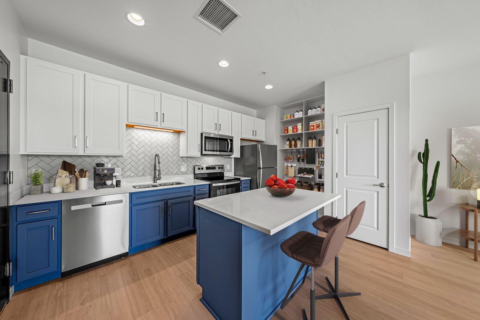 Modern apartment kitchen with blue lower cabinets, white upper cabinets, stainless steel appliances and an island.