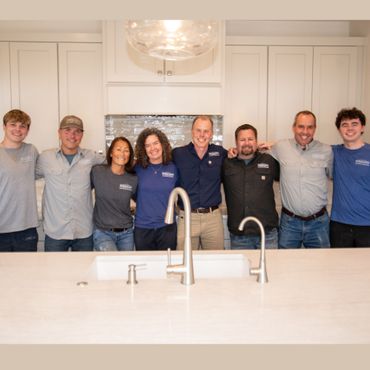 A group of people posing for a picture in front of a kitchen sink