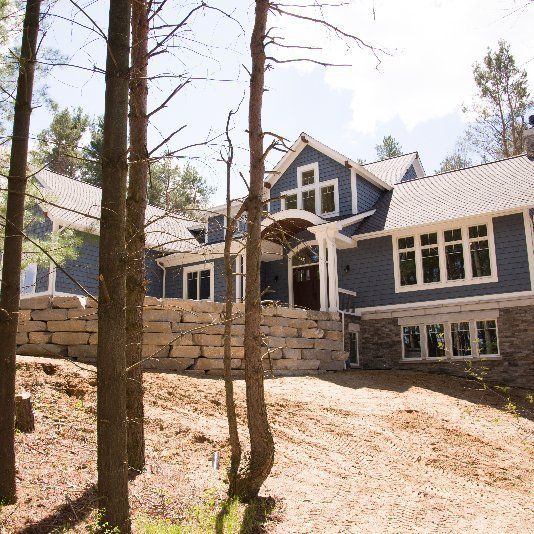 A large blue house is surrounded by trees and dirt