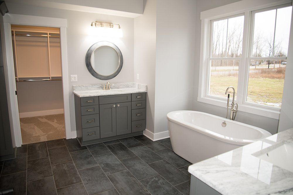 A bathroom with a tub , sink , mirror and window.