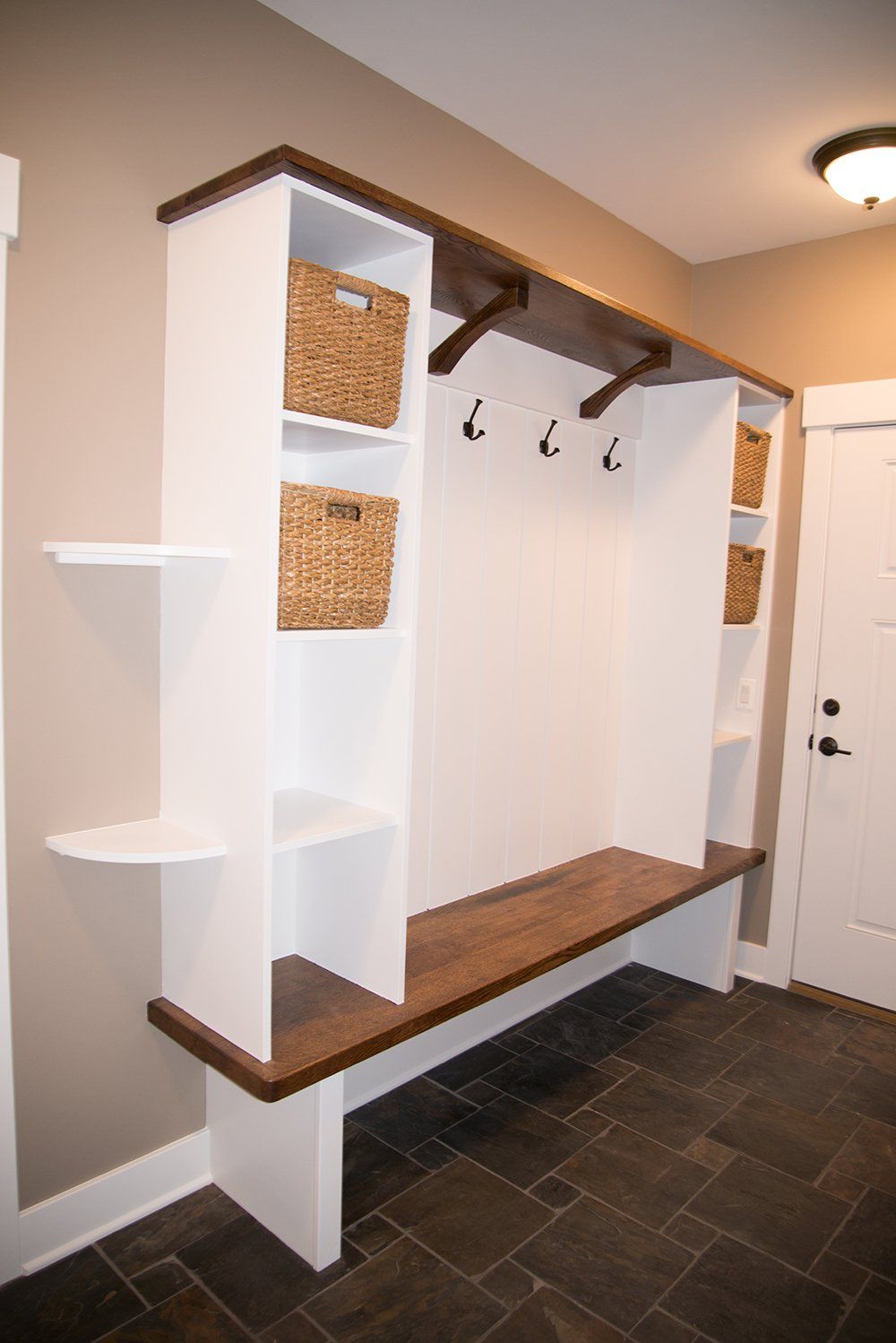 A hallway with a bench , shelves , hooks and baskets.