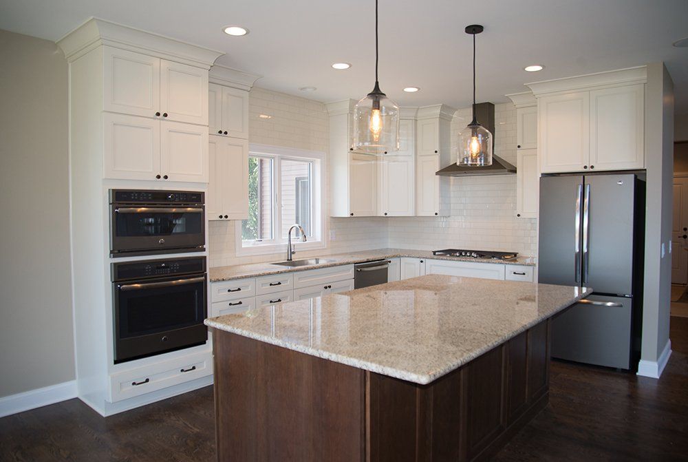 A kitchen with white cabinets , granite counter tops , stainless steel appliances and a large island.
