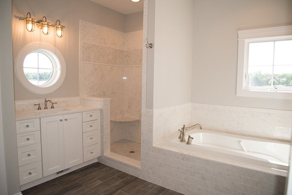 A bathroom with a tub , sink , shower and window.