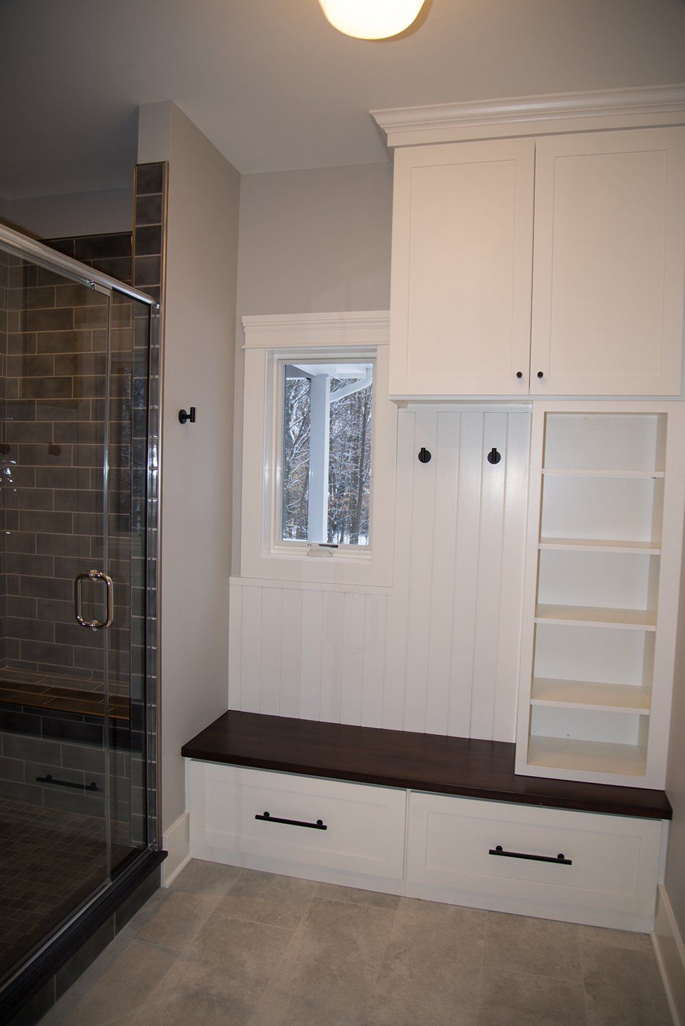A bathroom with a bench , shelves , and a shower.