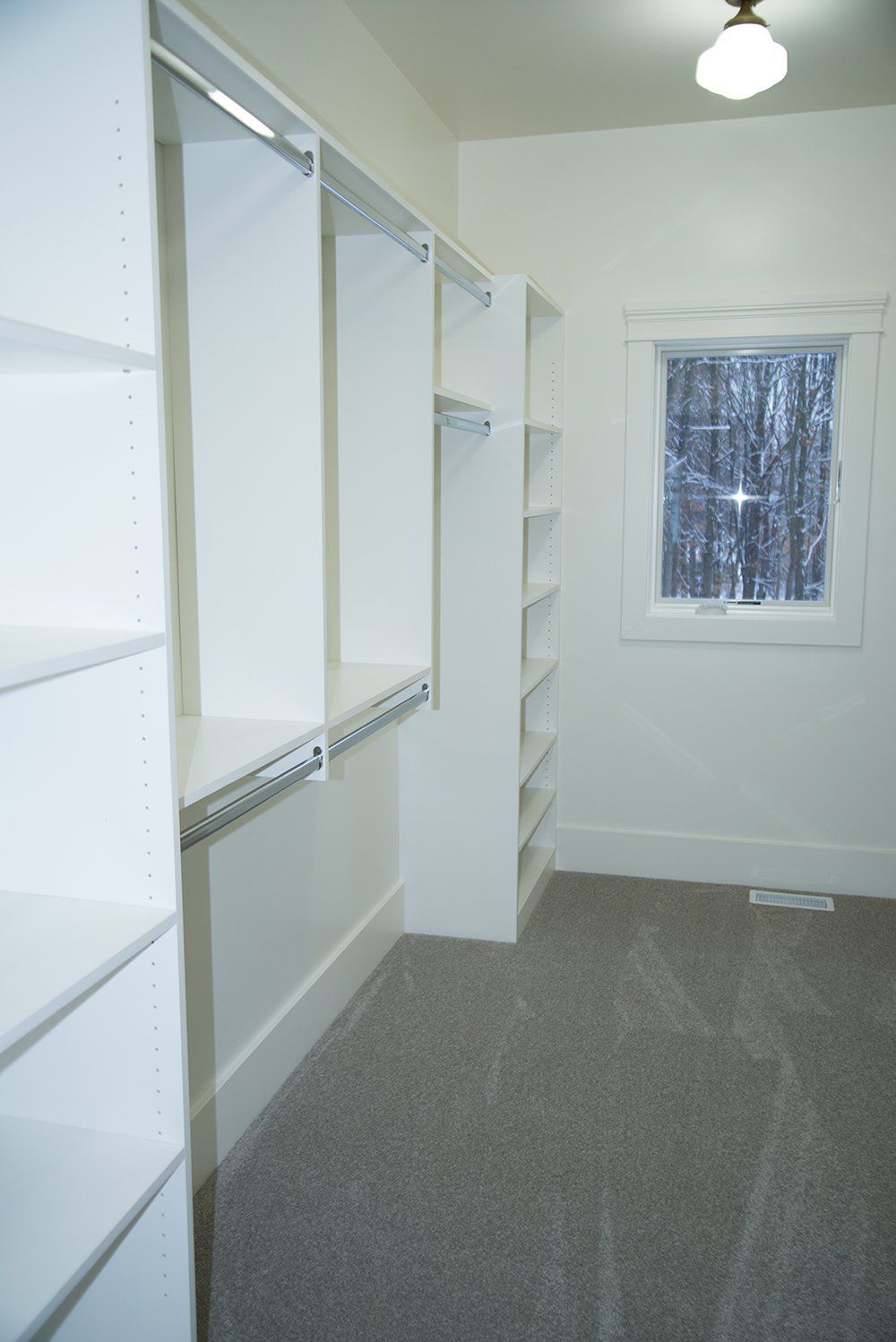 A walk in closet with white shelves and a window.