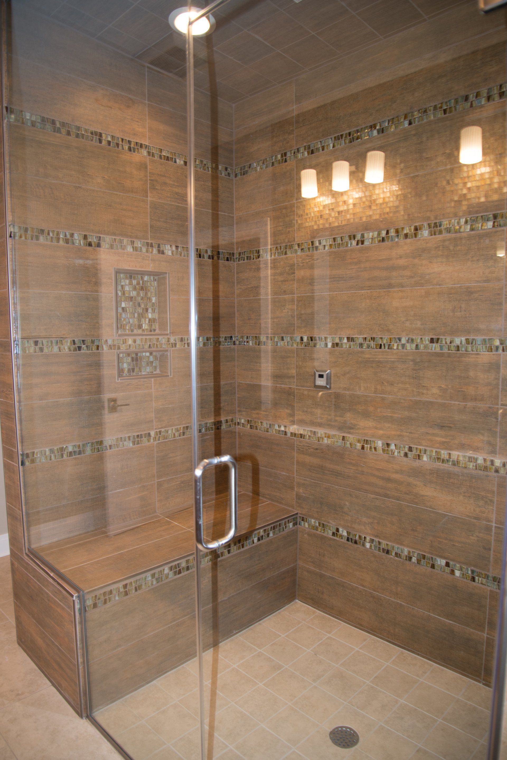 A walk in shower with a glass door and a bench.