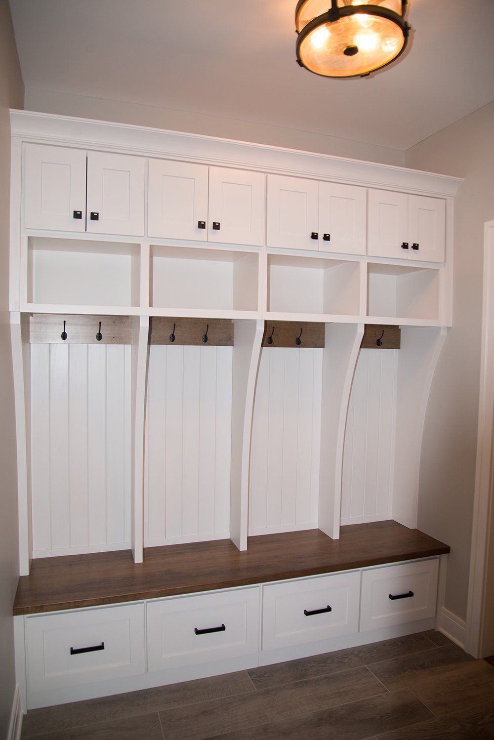 A mud room with white cabinets and drawers and a wooden bench.