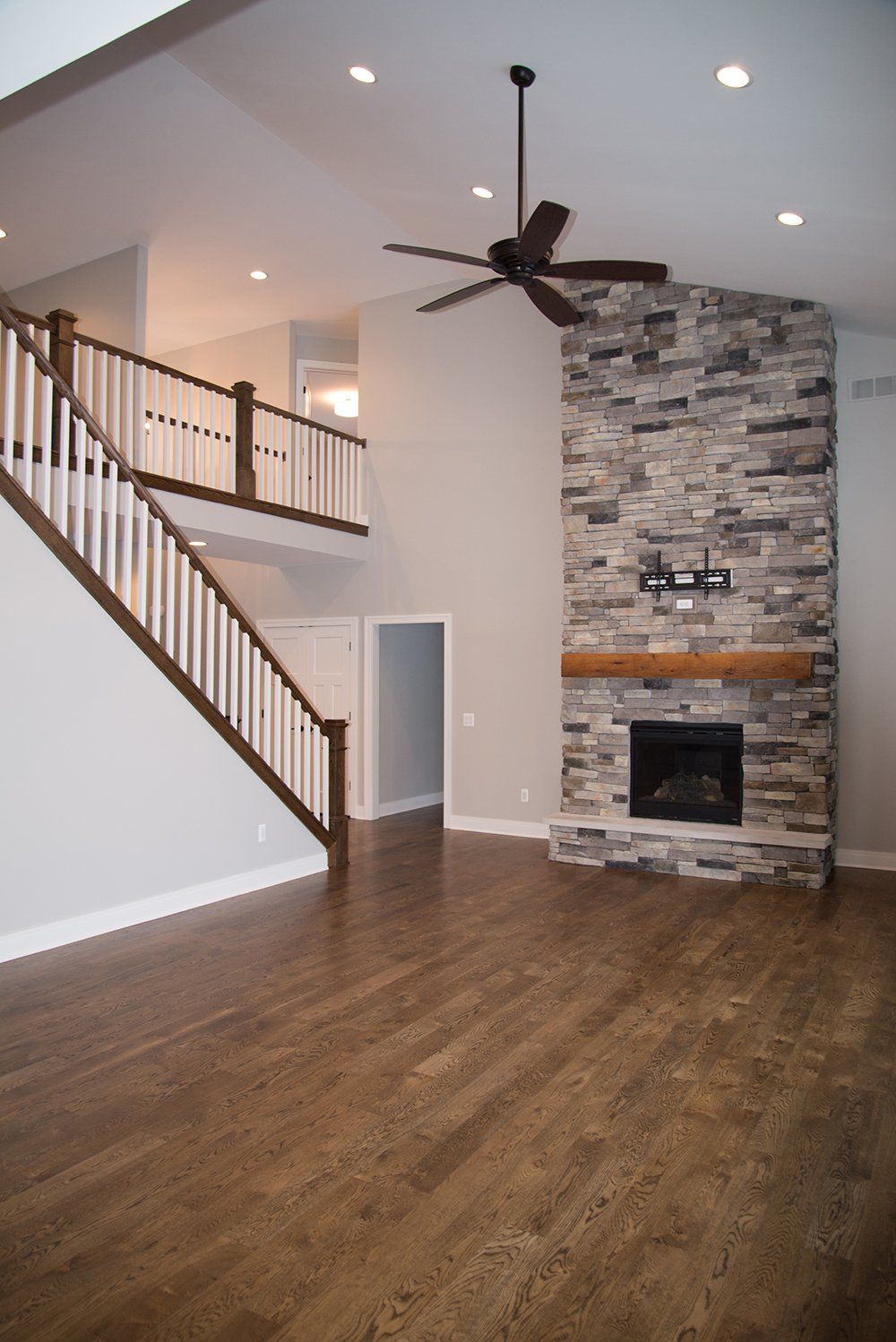 An empty living room with a stone fireplace and stairs.