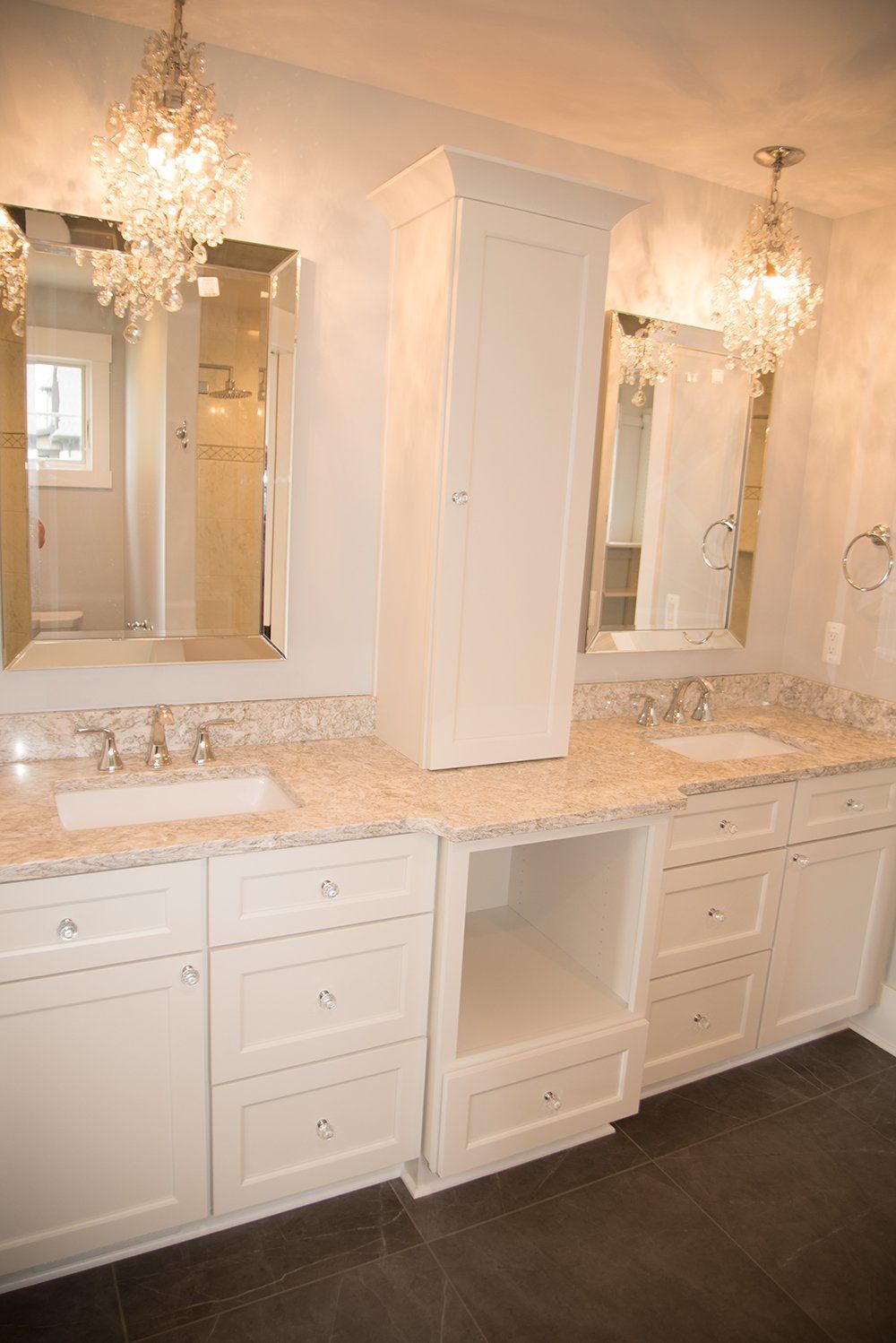 A bathroom with two sinks , two mirrors and a chandelier.