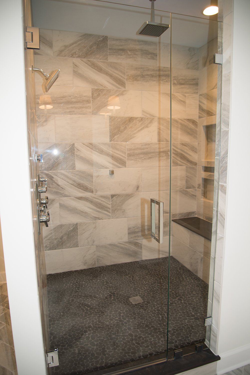 A shower with a glass door and marble tiles on the wall.
