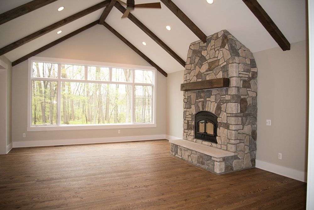 An empty living room with a stone fireplace and a large window.