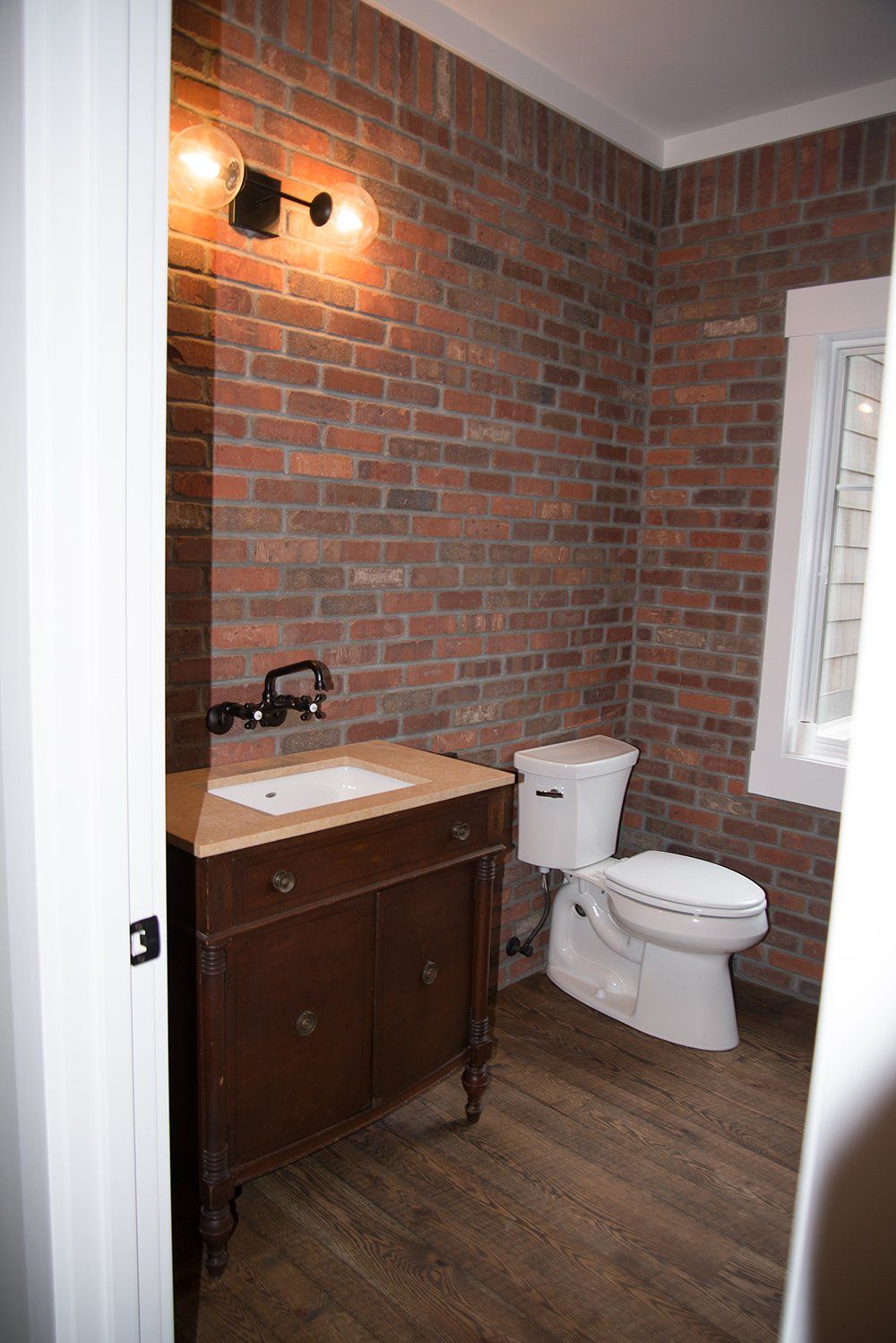 A bathroom with a toilet , sink and brick wall.