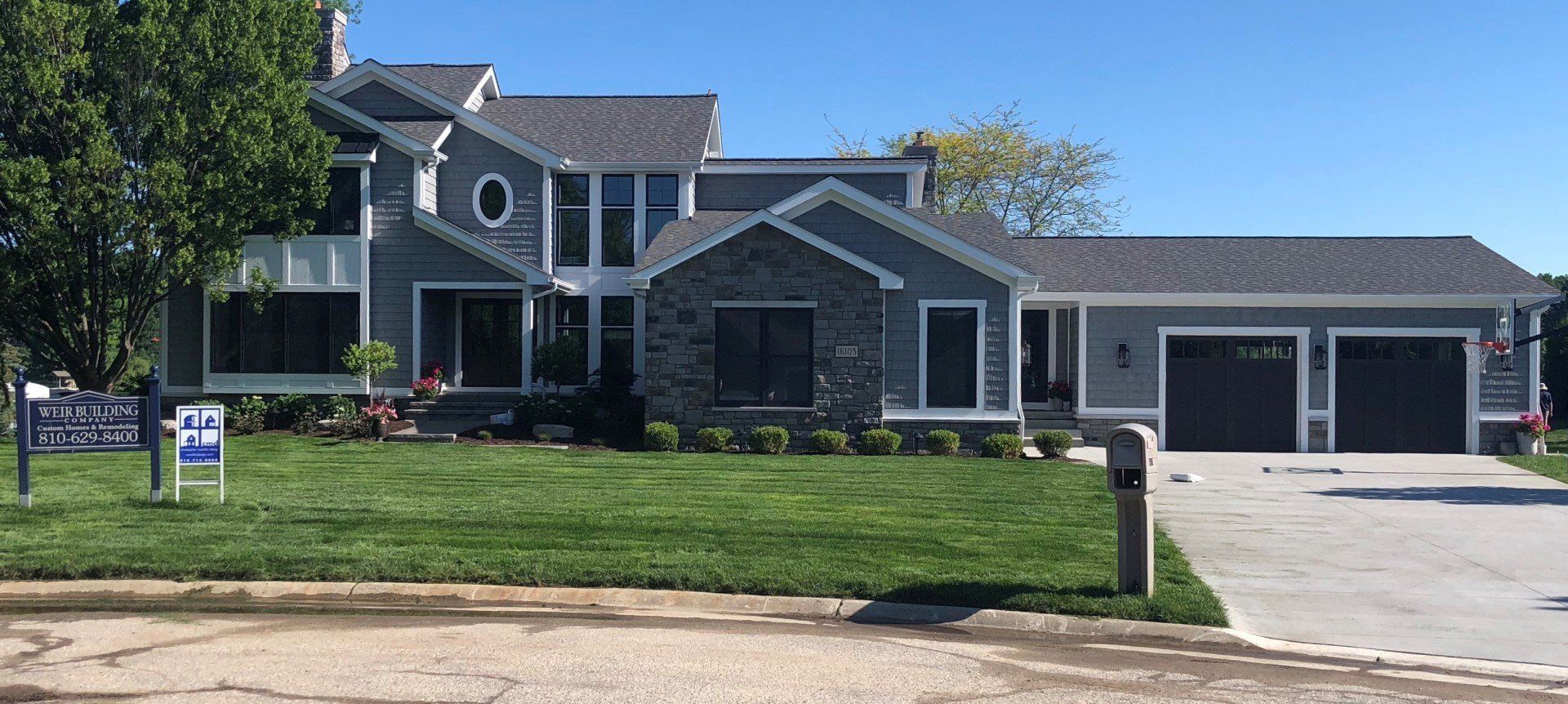 A large gray house with a for sale sign in front of it.