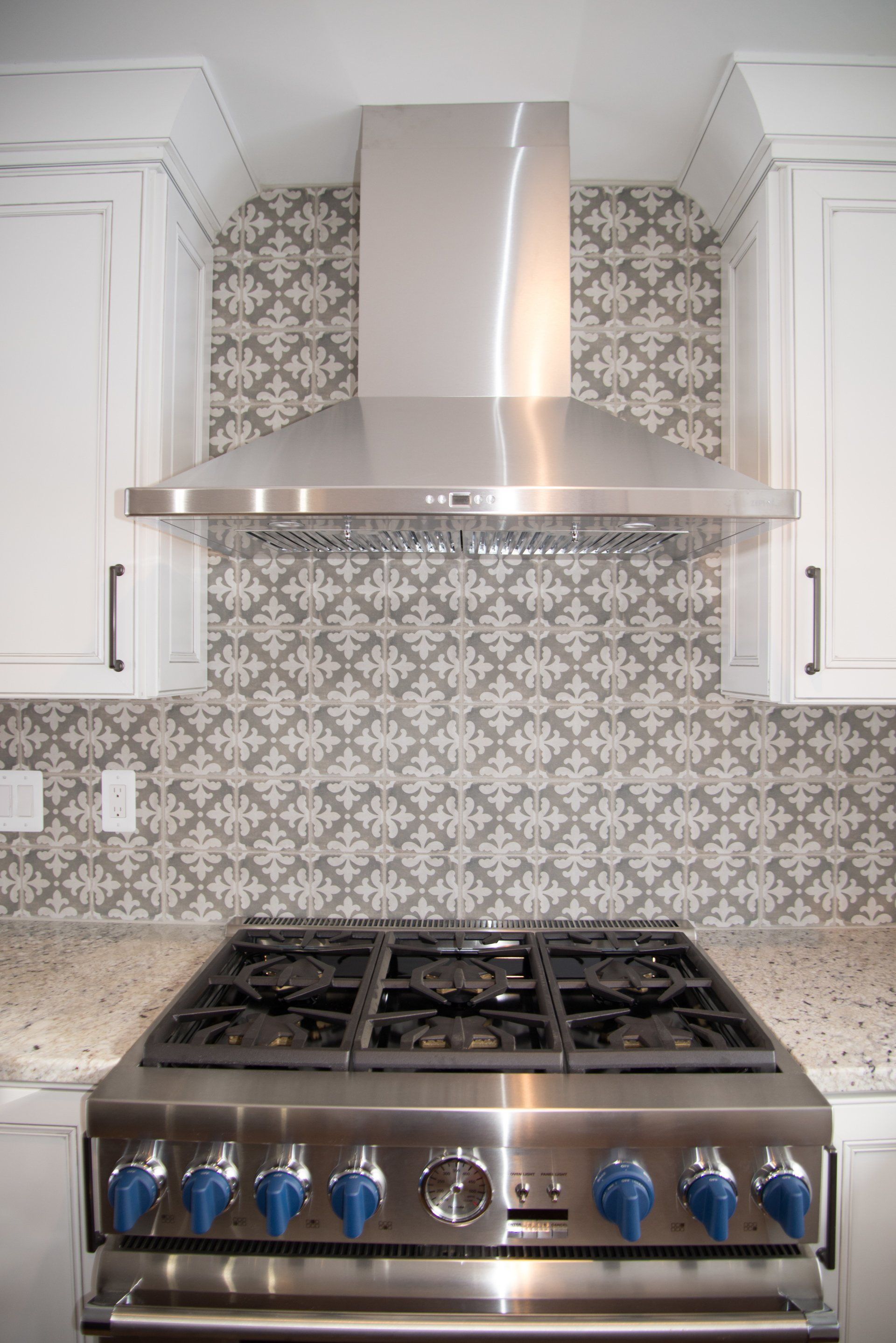 A stainless steel stove top oven with blue knobs and a hood in a kitchen.