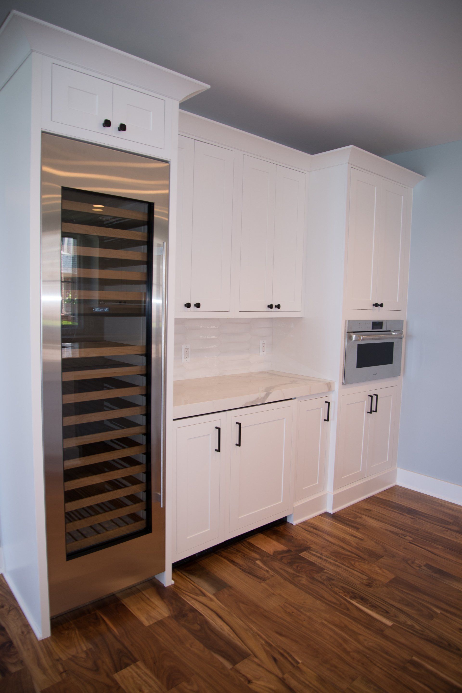 A kitchen with white cabinets and a stainless steel wine cooler.