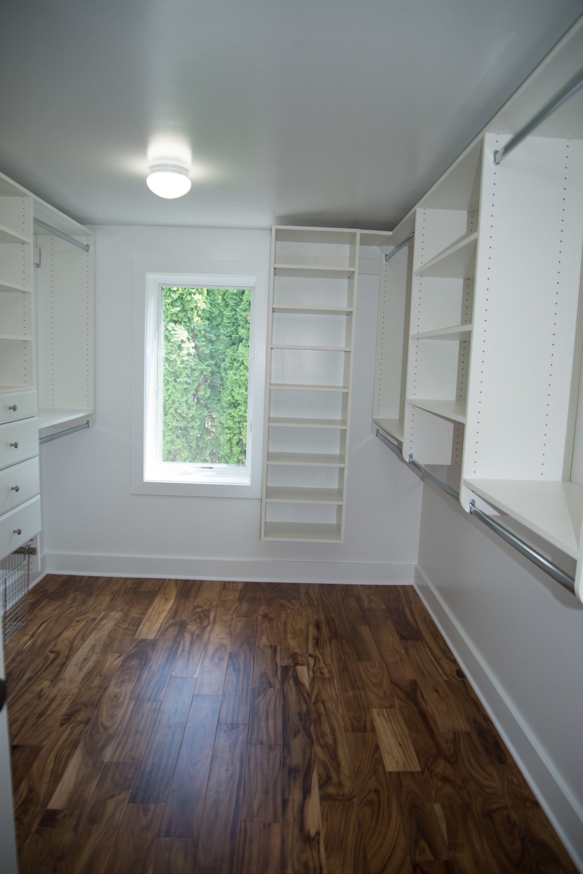 A walk in closet with hardwood floors and white shelves.