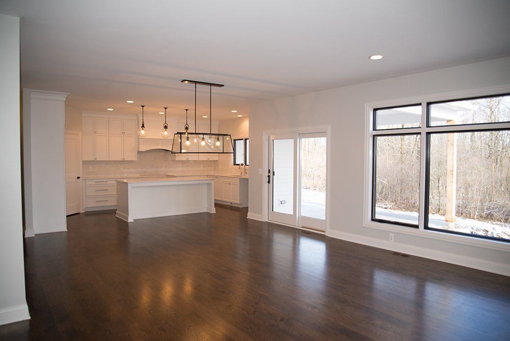 An empty living room with hardwood floors and a kitchen in the background.
