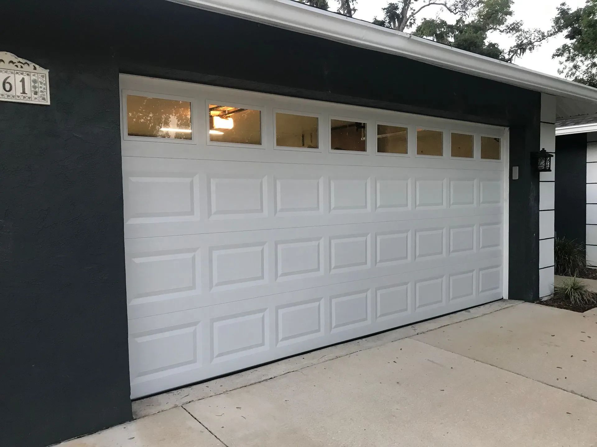 White garage door with glass upper panels on a dark gray house.