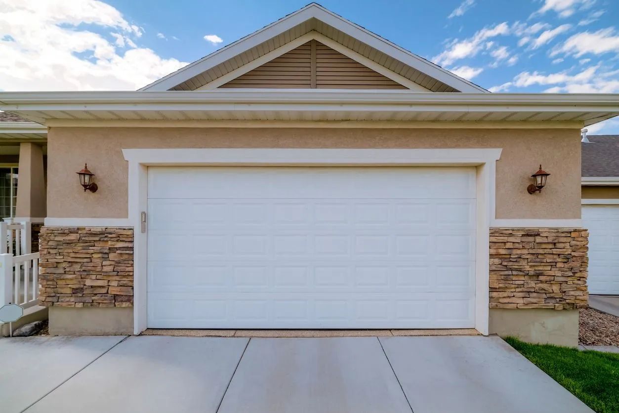 White garage door on beige house with stone accents, concrete driveway, and blue sky.