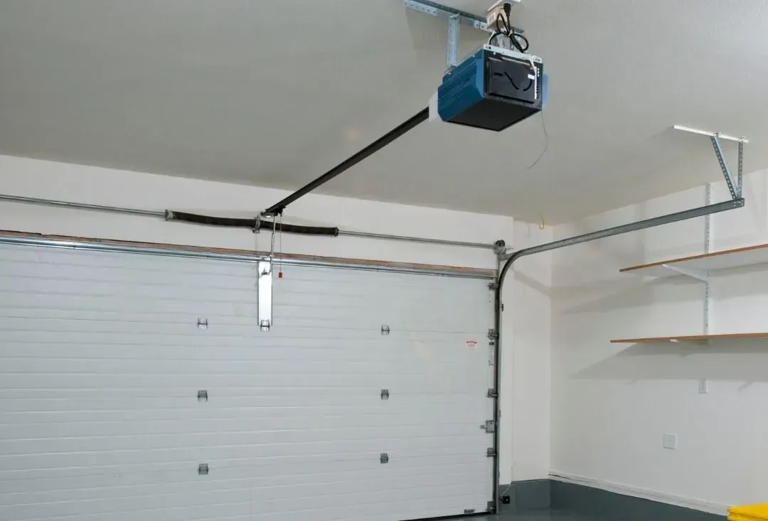 A garage door opener is hanging from the ceiling above a garage door.