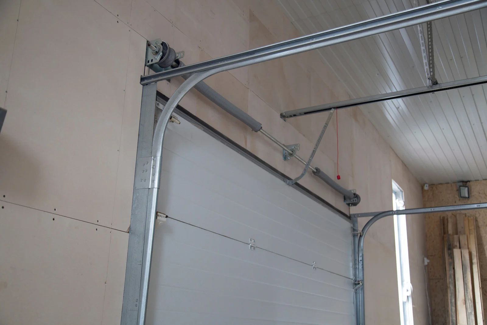 Garage door, white panels, gray frame and tracks, mounted on a beige wall.