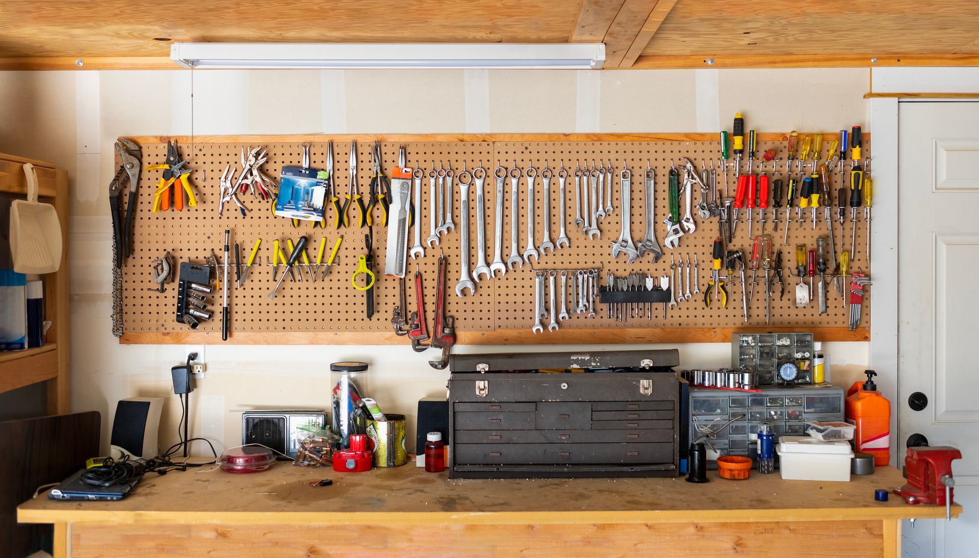 A workbench in a garage with lots of tools hanging on the wall.