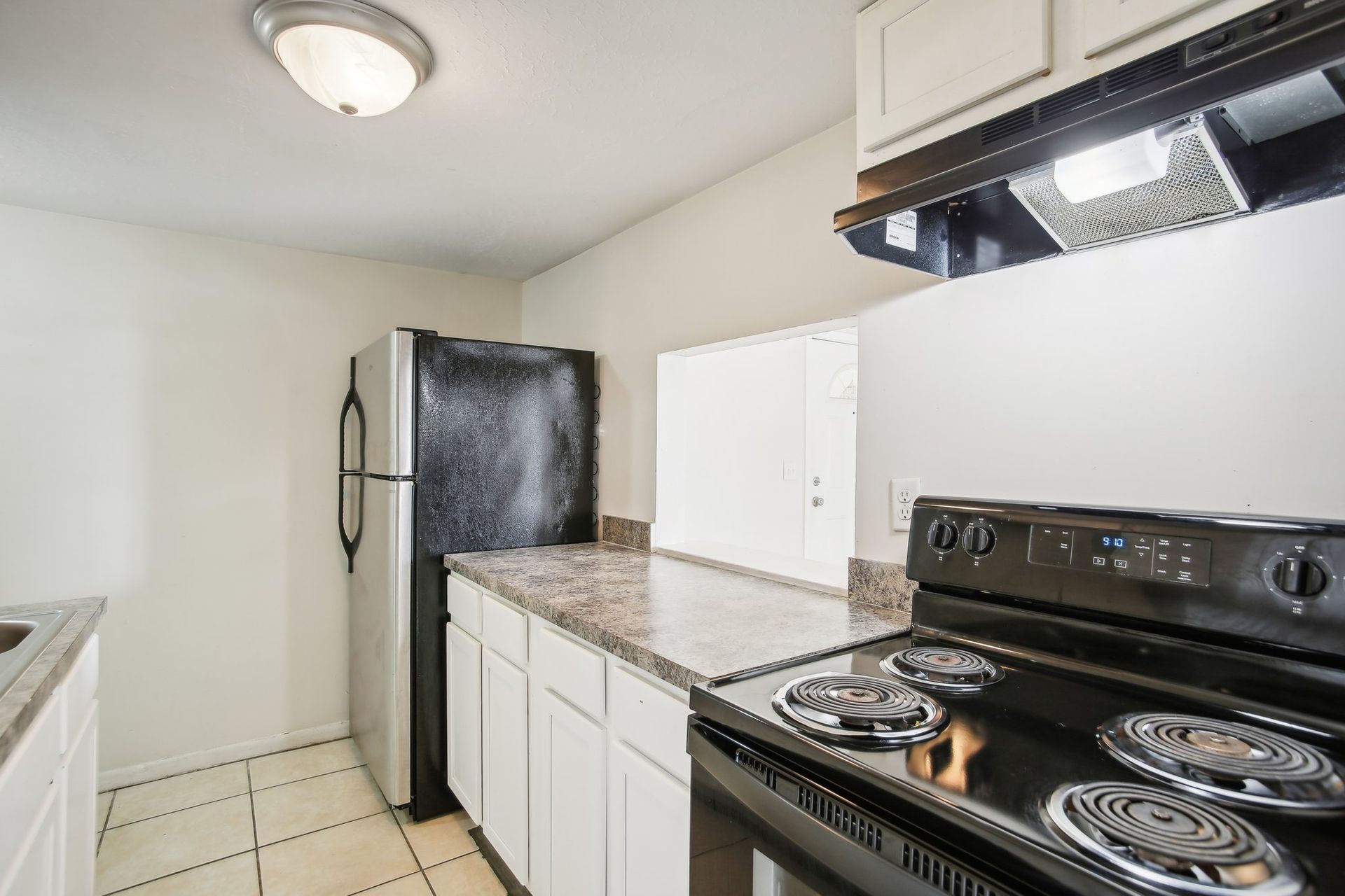 Kitchen with black appliances, white cabinets, and speckled countertops.