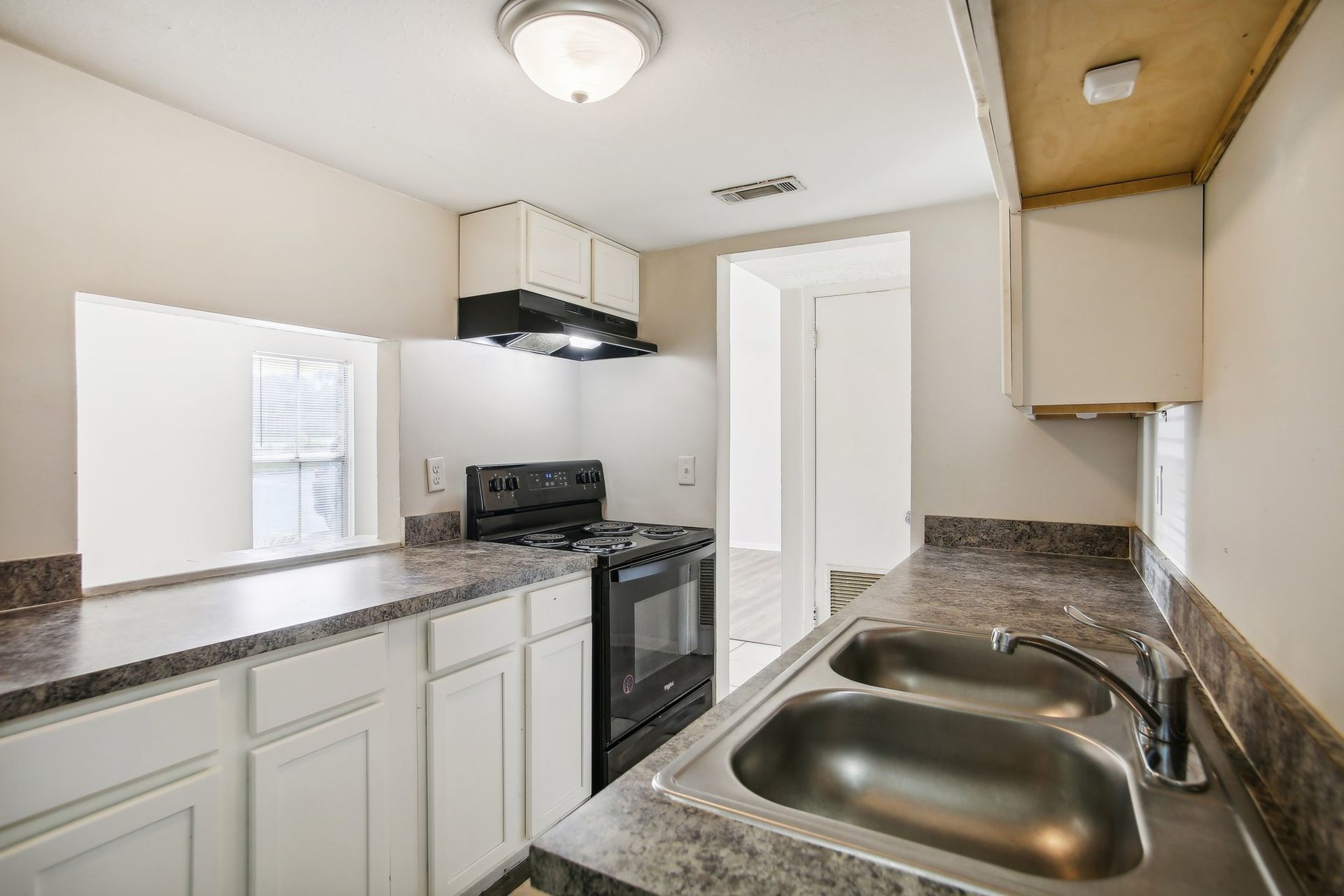 Kitchen with white cabinets, dark stovetop, and double sink. Countertops are a dark speckled color.
