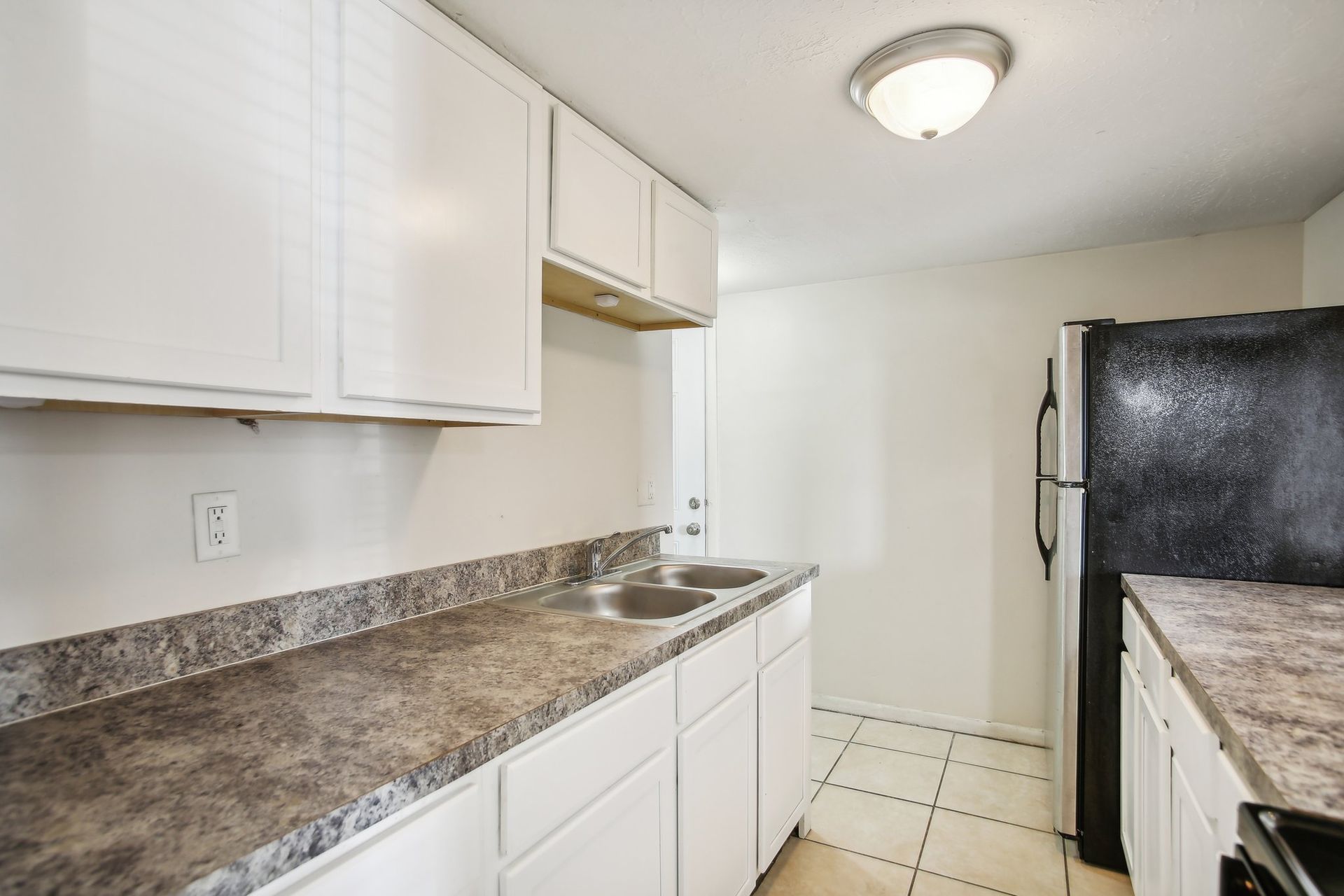 Kitchen with white cabinets, dark countertops, and a black refrigerator.