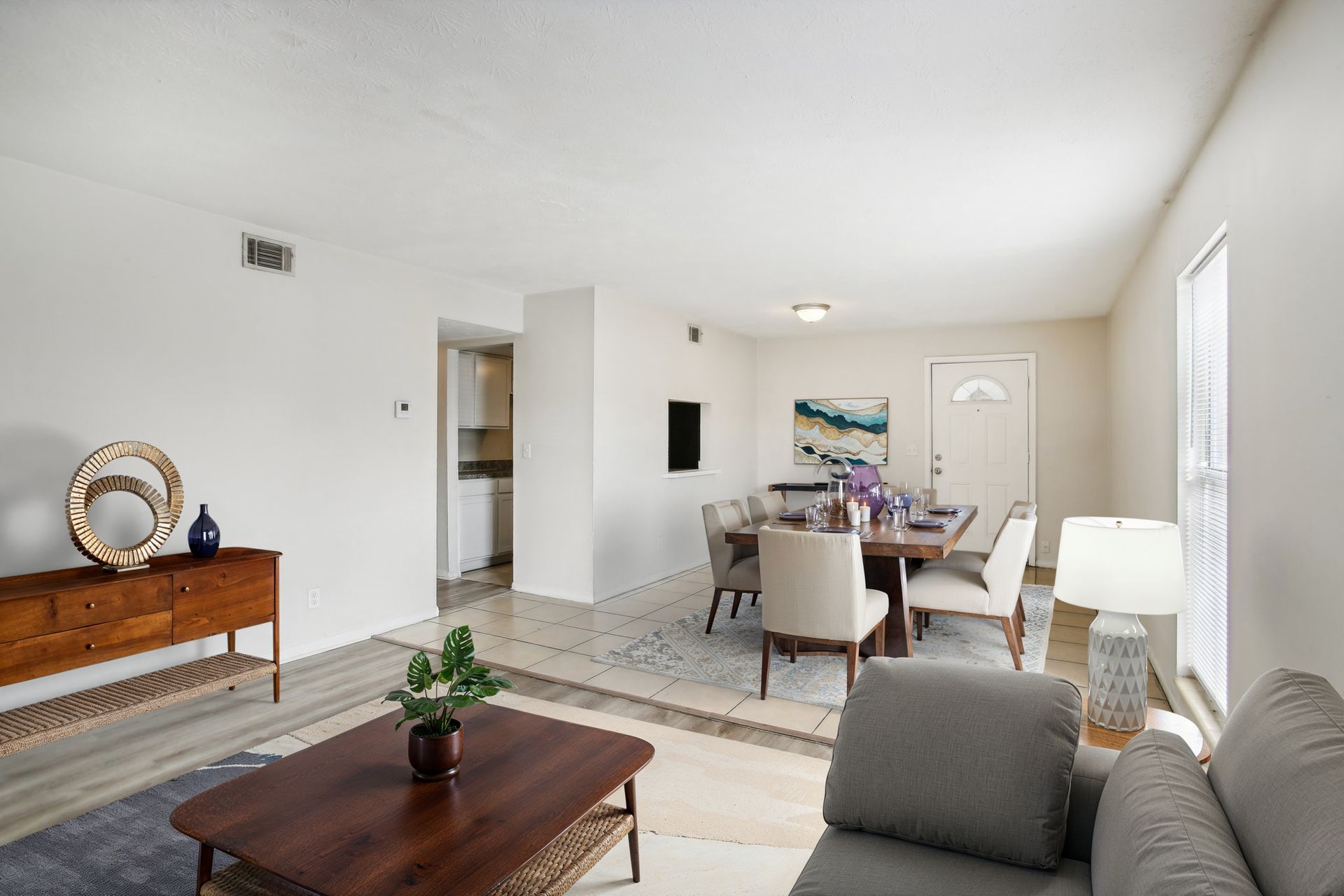Living room with dining area. White walls, wooden console, dark coffee table, dining table with chairs, gray sofa.