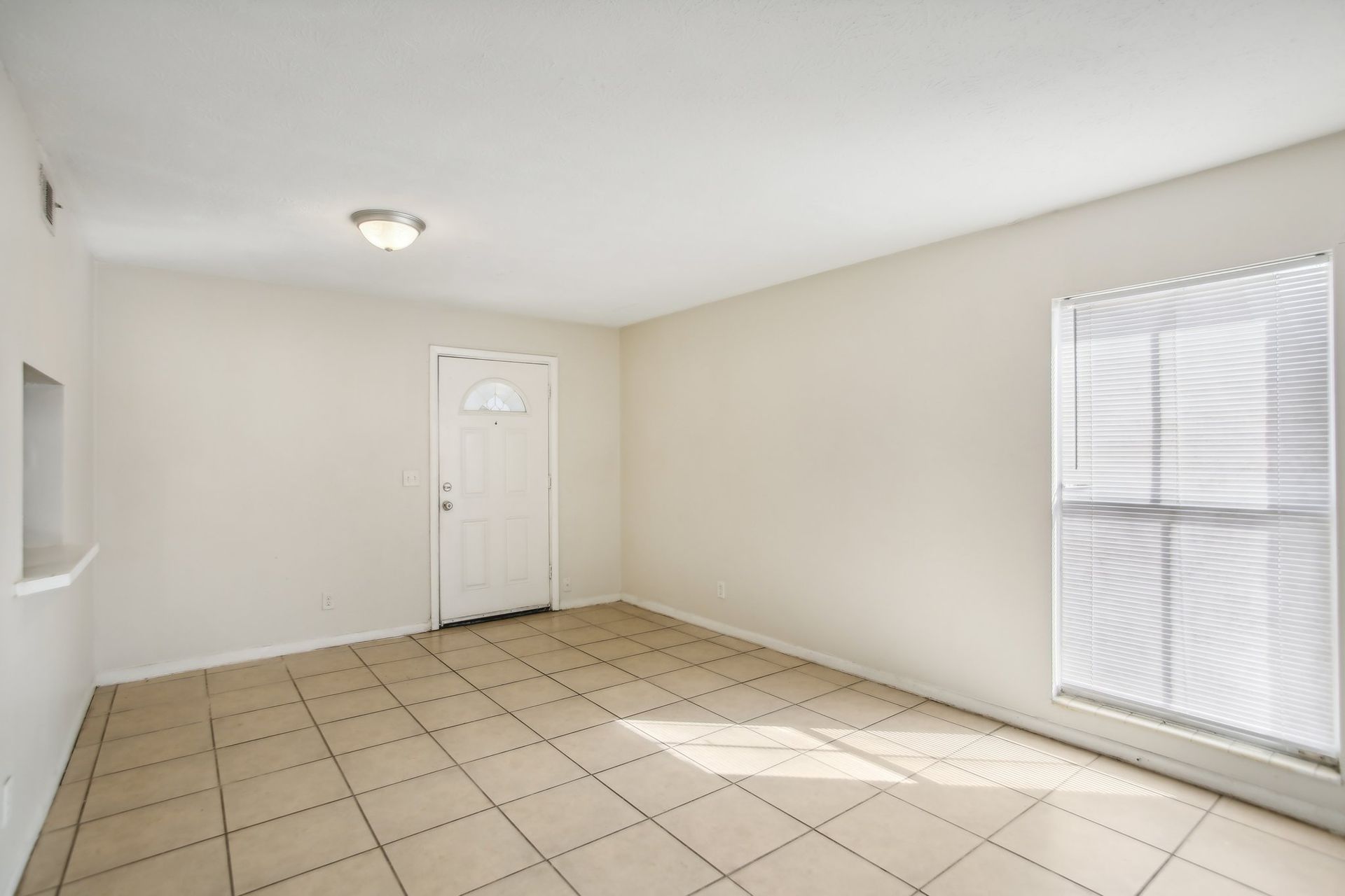 Empty room with tan tiled floor, white walls, door, and window.