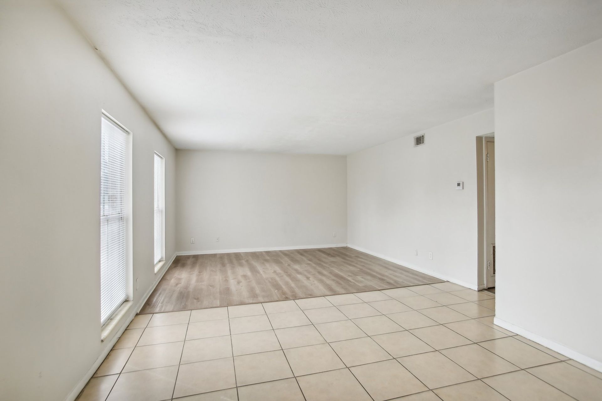 Empty room with tile floor, wood-look flooring, windows, and white walls.