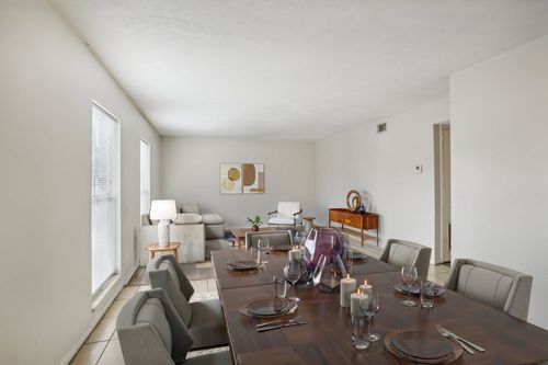 Dining room with long wooden table set for meal, chairs, and living area with sofa and art on wall.