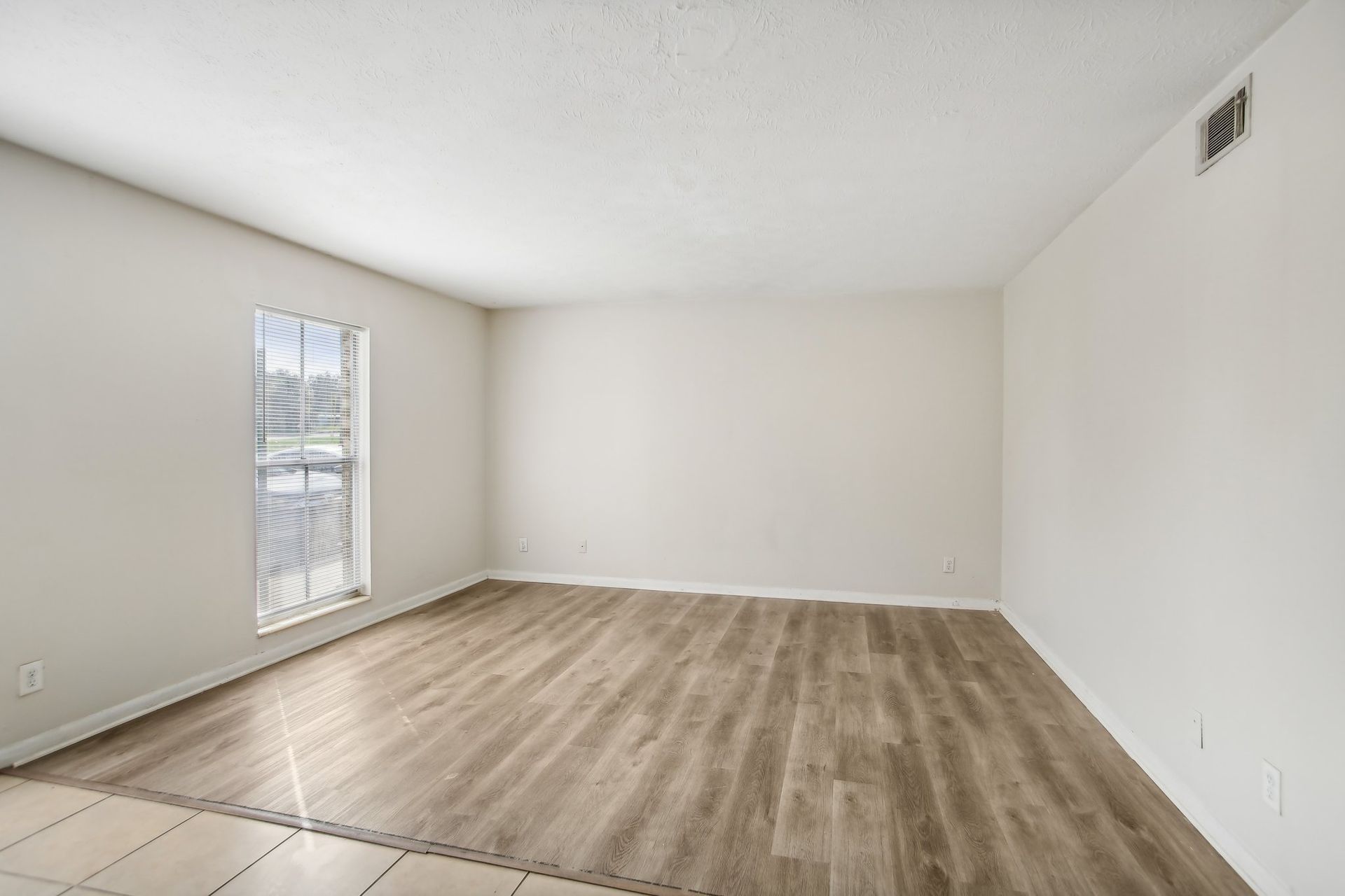Empty room with light wood-look flooring, white walls, and a window with blinds.