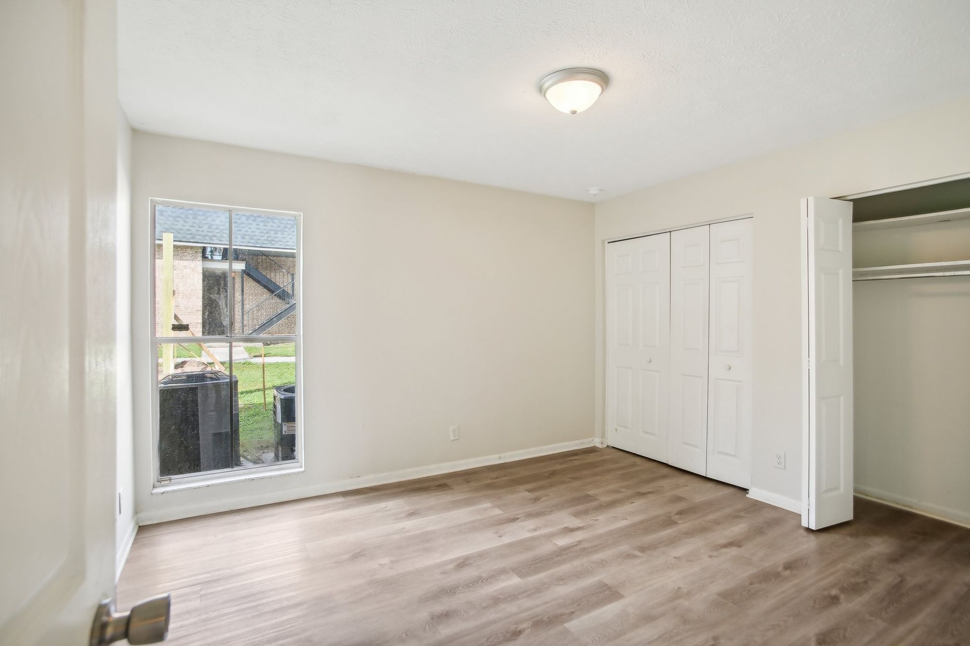Empty room with window, closet, and wood-look flooring. Light walls and ceiling.
