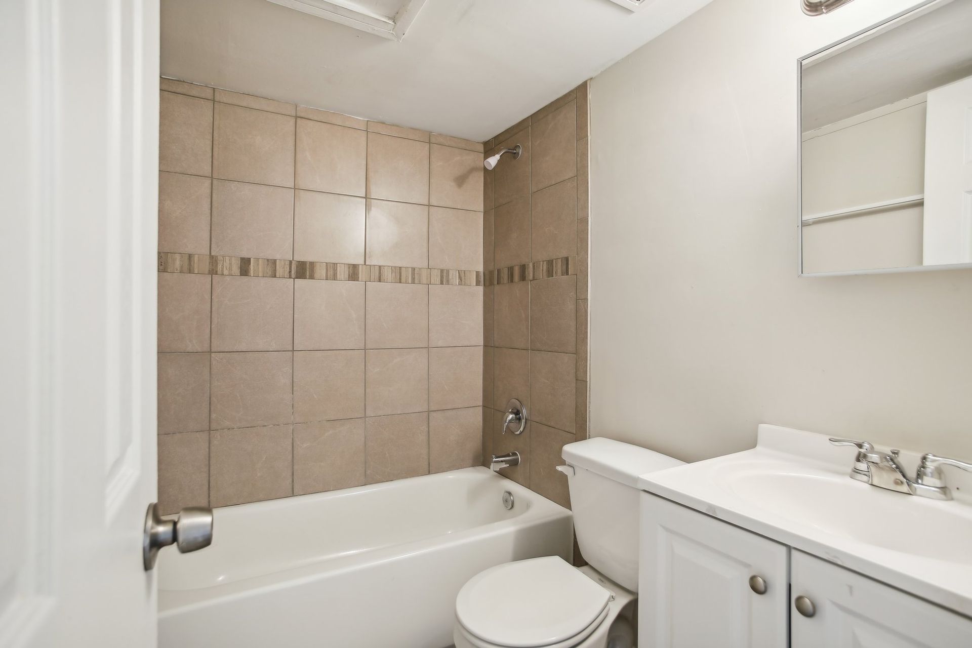 Bathroom with white fixtures, beige tiled shower wall, and white cabinet.