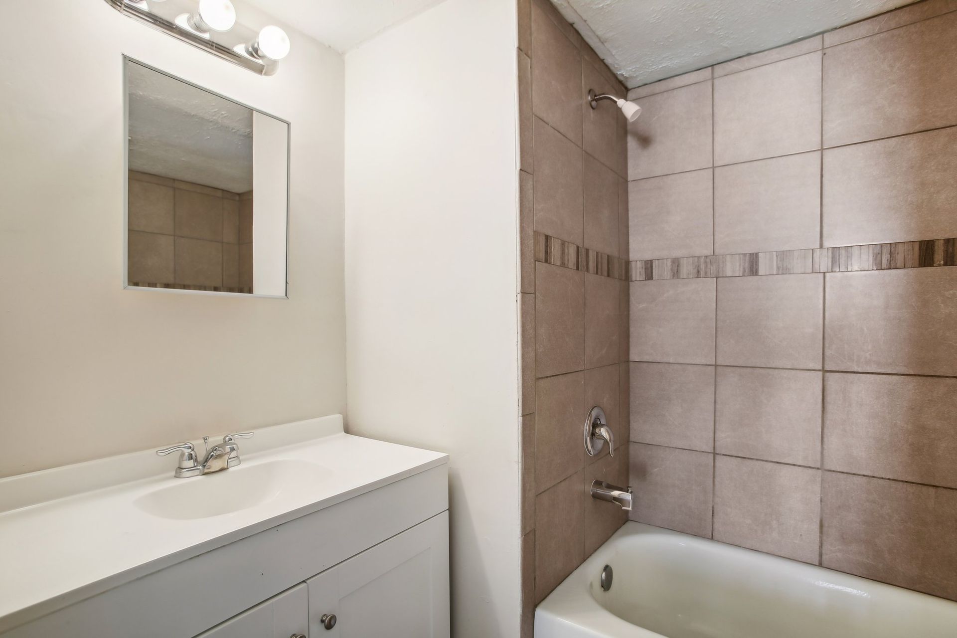Bathroom with white vanity, tan tiled shower, and mirror.