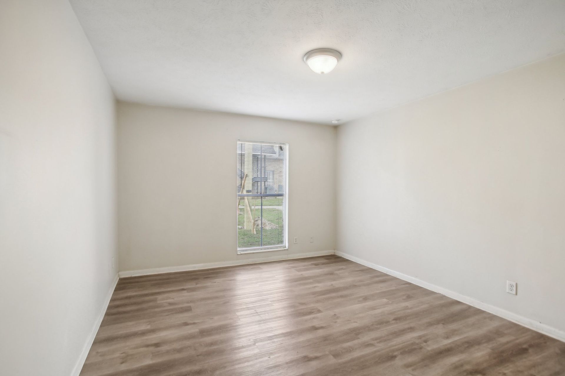 Empty room with light wood-look floor, off-white walls, and a small window.