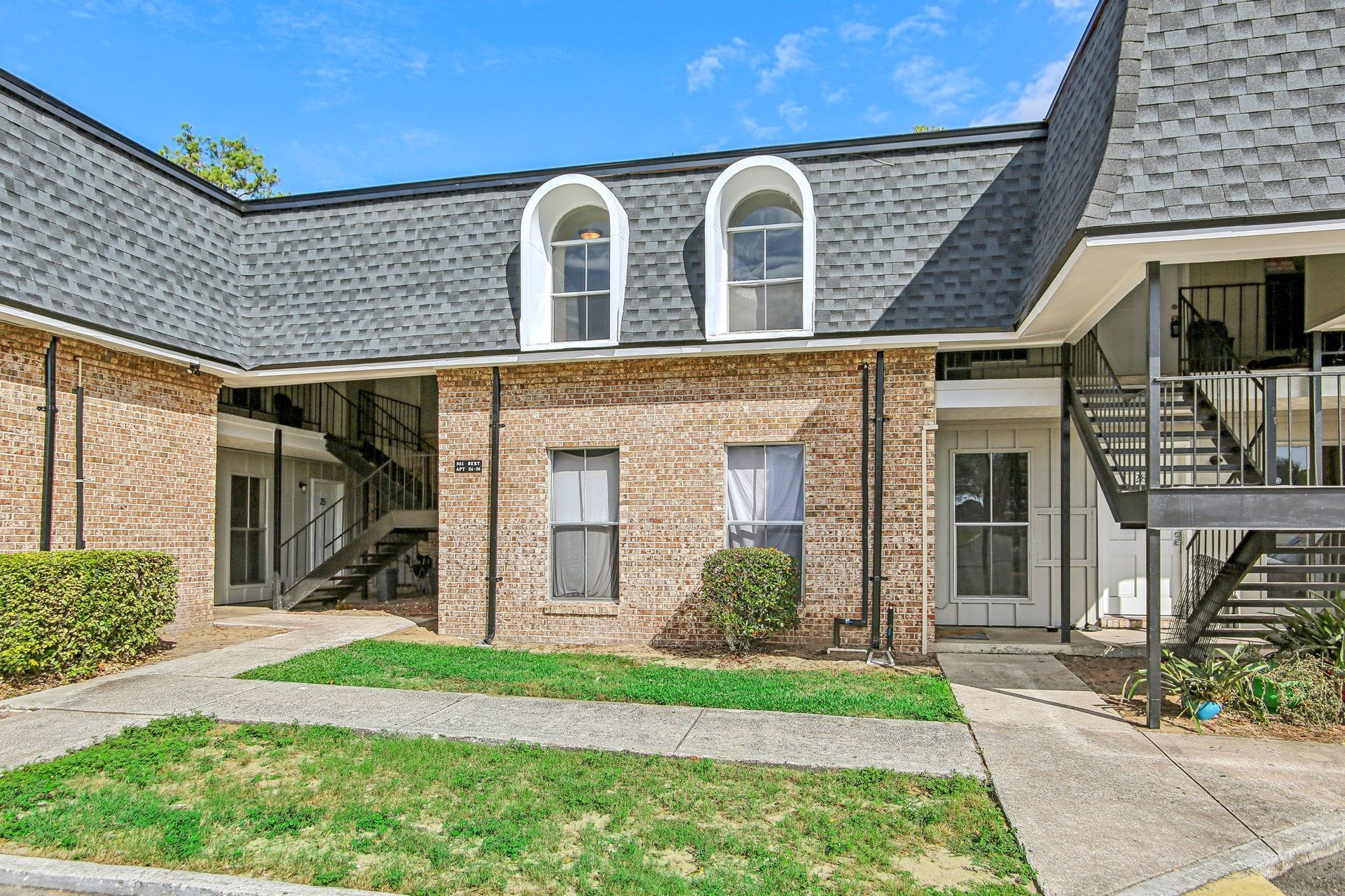 Two-story brick apartment building with dark gray roof, two arched windows. Front walkway, stairs.