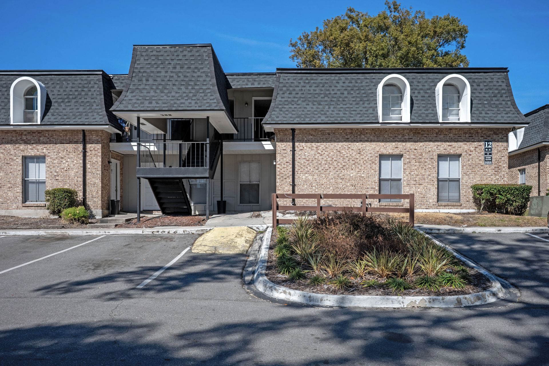 Apartment building with brick exterior, black roof, and parking lot on a sunny day.