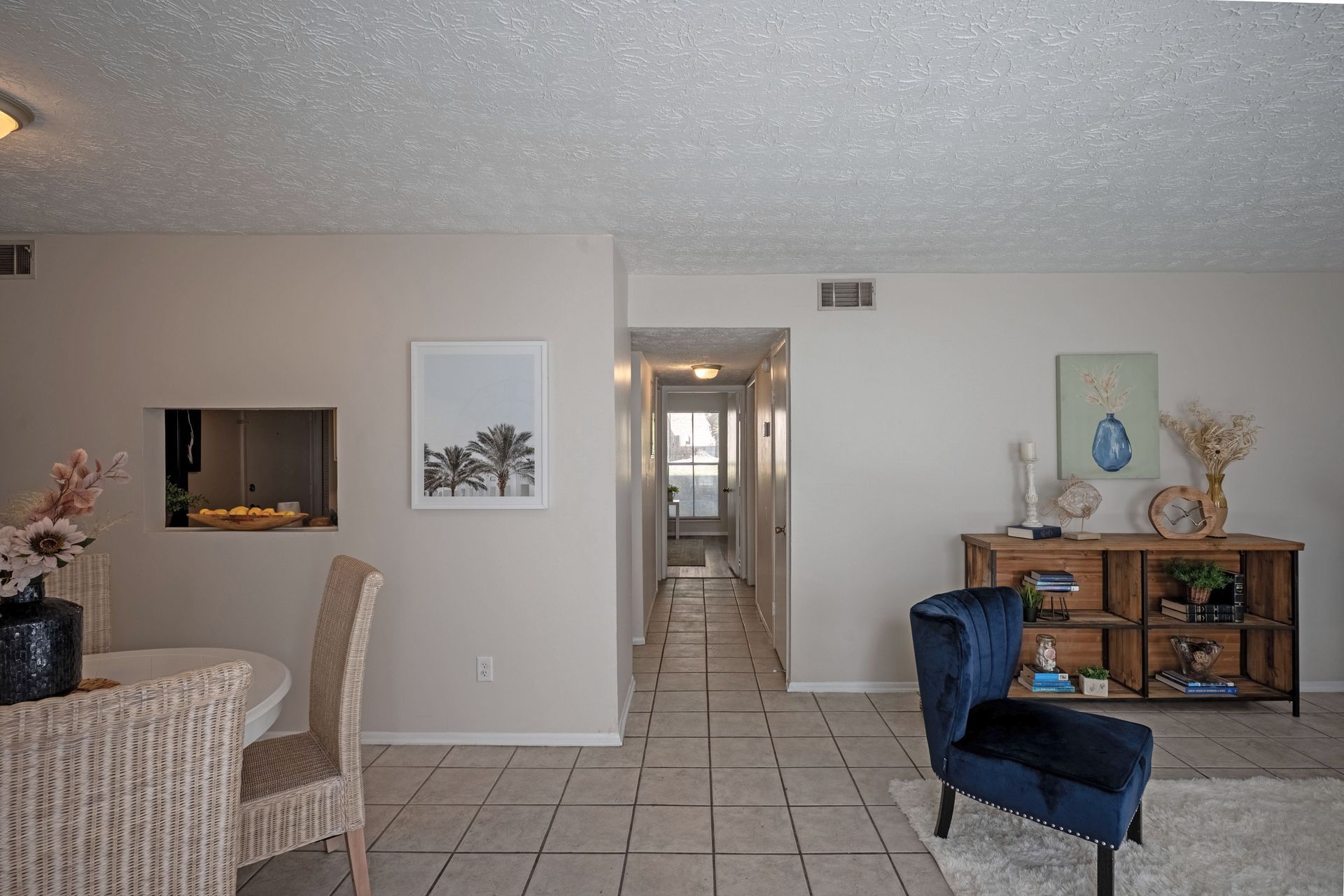 Living room with hallway view: beige walls, tiled floor, a blue chair, and wood console.