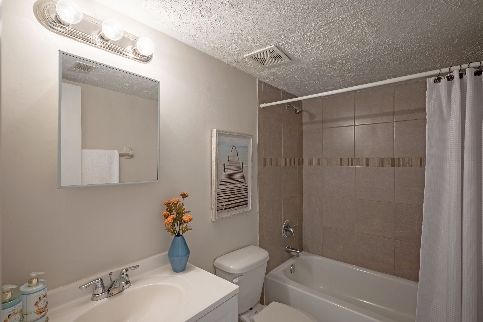 Bathroom with white sink, toilet, tub, and beige tiled walls. Includes mirror and decorative items.