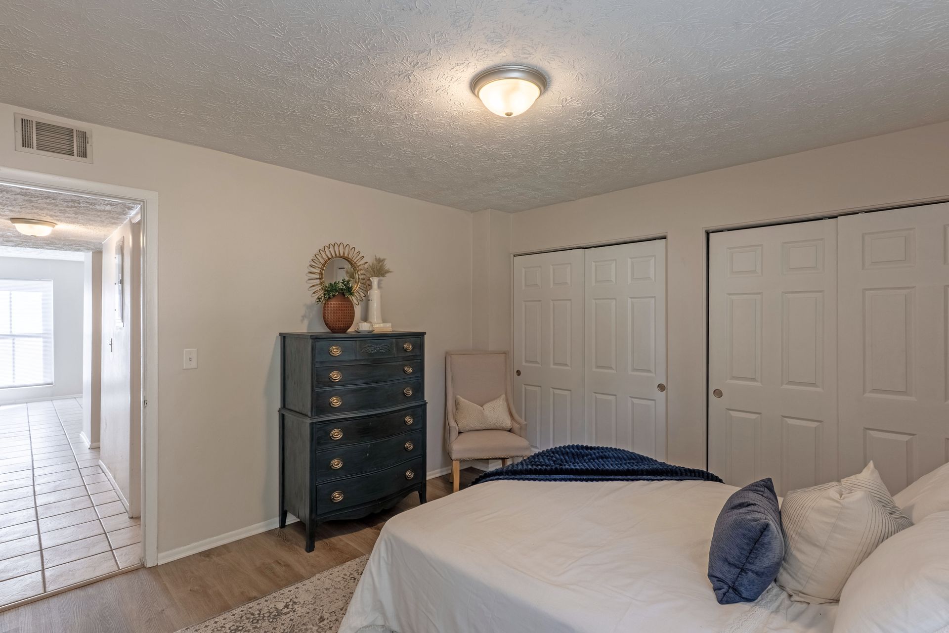 Bedroom interior with bed, chest of drawers, closet, and a doorway leading to another room.