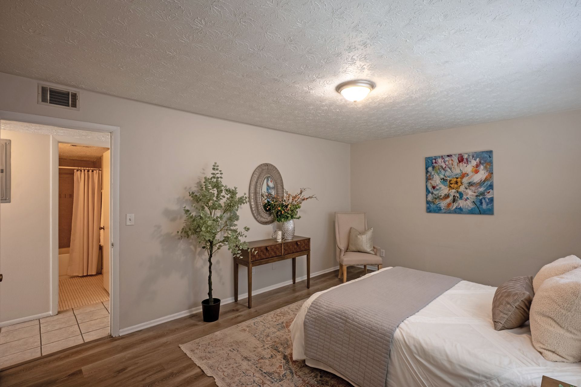 Bedroom with bed, chair, console table, and artwork; a doorway leads to a bathroom.