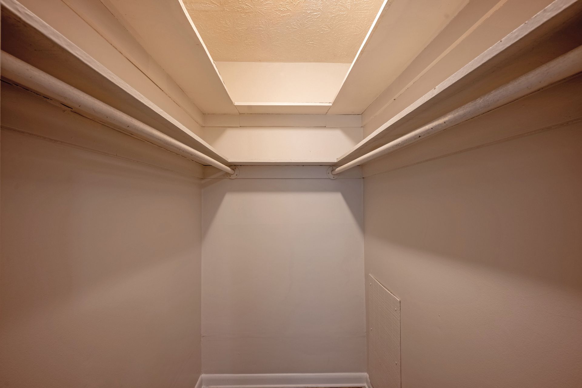 Empty walk-in closet with shelves and a clothing rod. Neutral walls and ceiling, natural light from above.