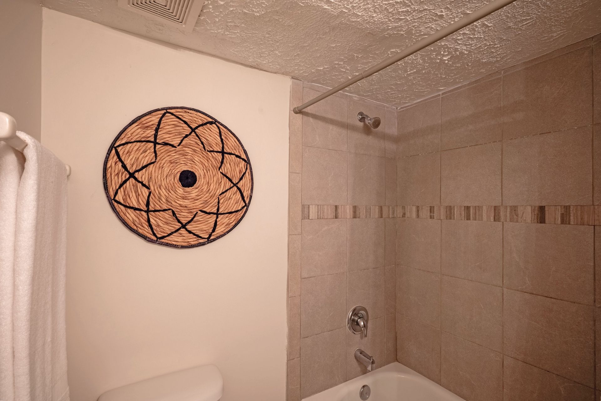 Bathroom interior with beige tile, shower, toilet, and decorative circular wall art.