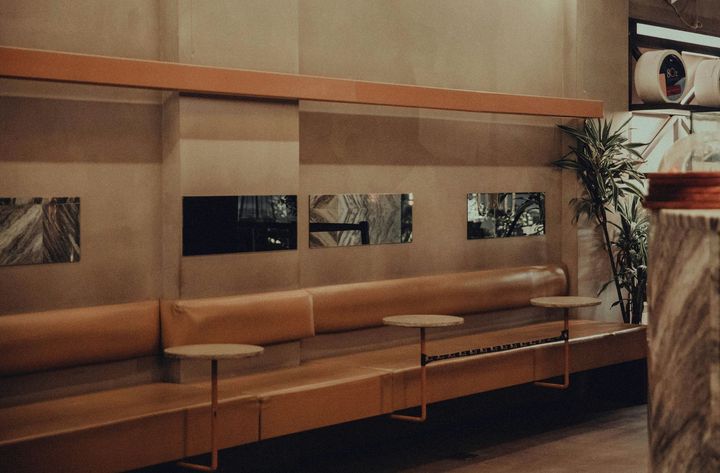 Brown leather booth seating in a cafe with small round tables, neutral walls, and mirrors.