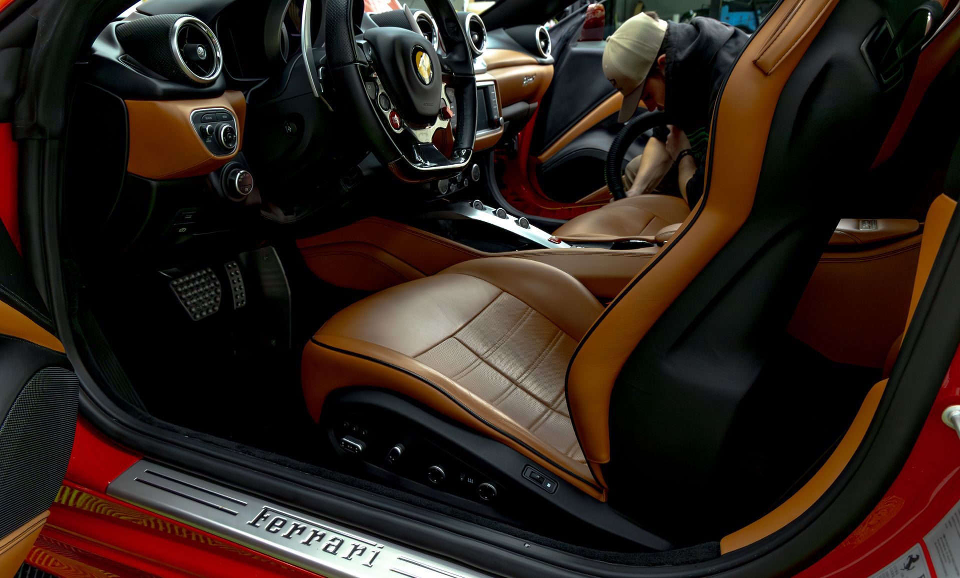 Interior view of a red Ferrari with tan and black leather seats. Door open.